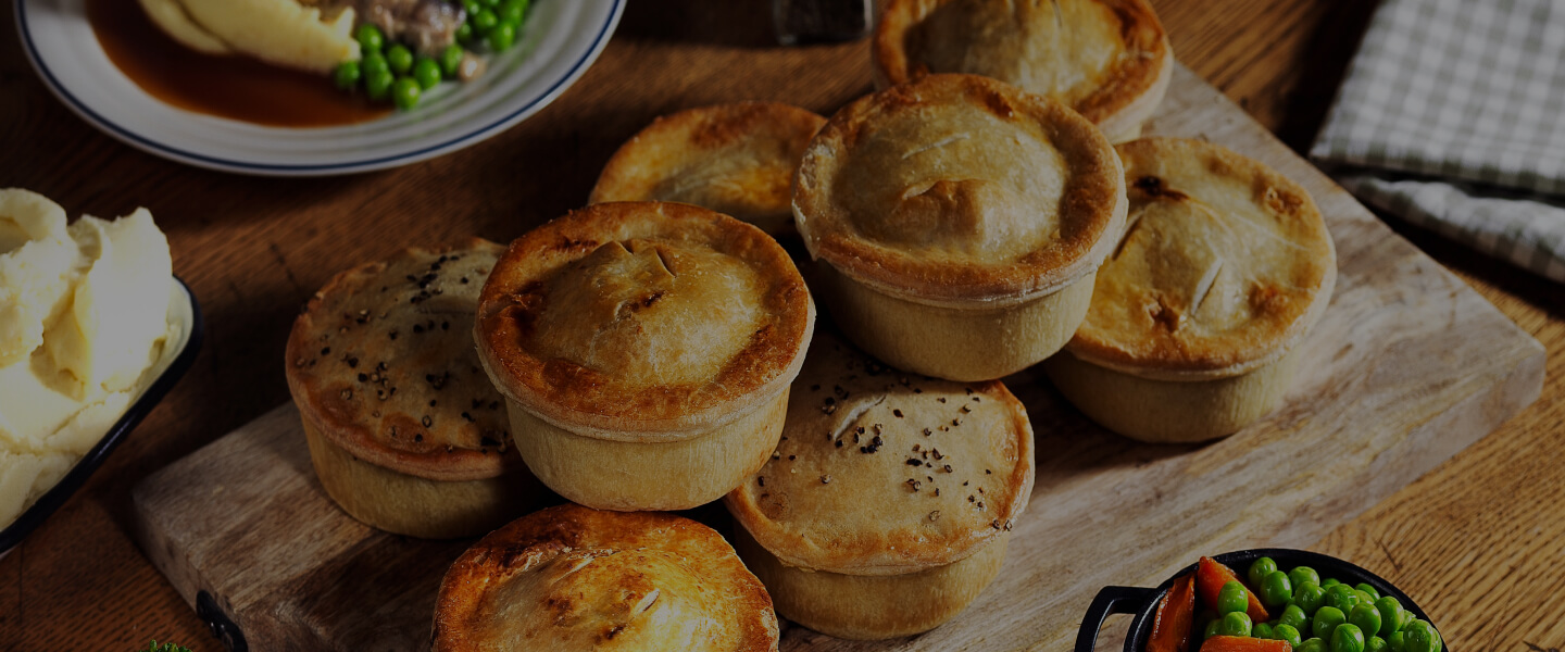 Table Table pies stacked on a wooden board with dishes of mashed potatoes and peas.