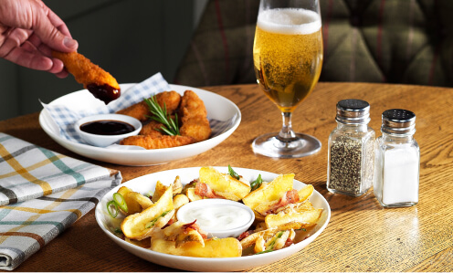 Table Table starters including chicken dippers and potato wedges on round plates with a small beer and salt and pepper shakers.