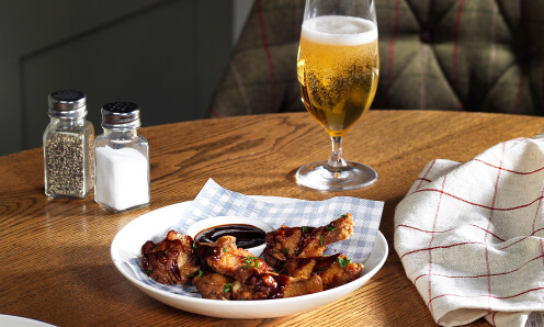 Chicken wings in a round bowl with salt and pepper shakers and a small beer on a table.