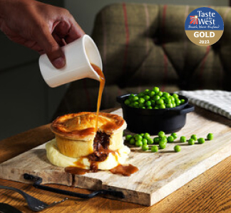 Table Table Beef and Ale Pie with gravy, peas and mashed potatoes on a wooden board.