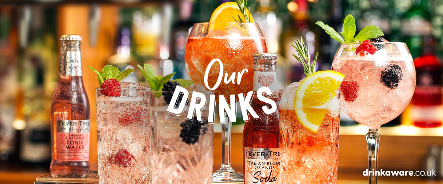 Table Table drinks menu items in different sized glasses with fruit garnishes and bottles of tonic water and soda.